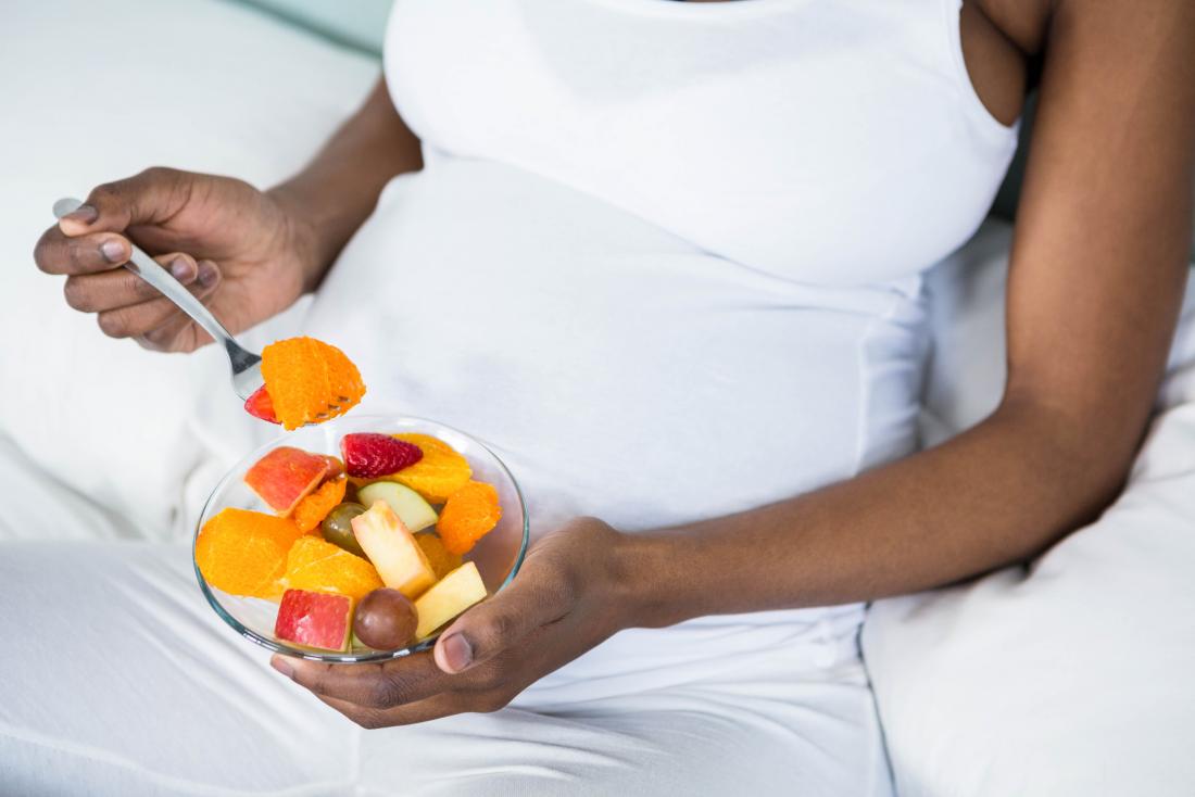 Wanita hamil makan mangkuk salad buah yang sihat.