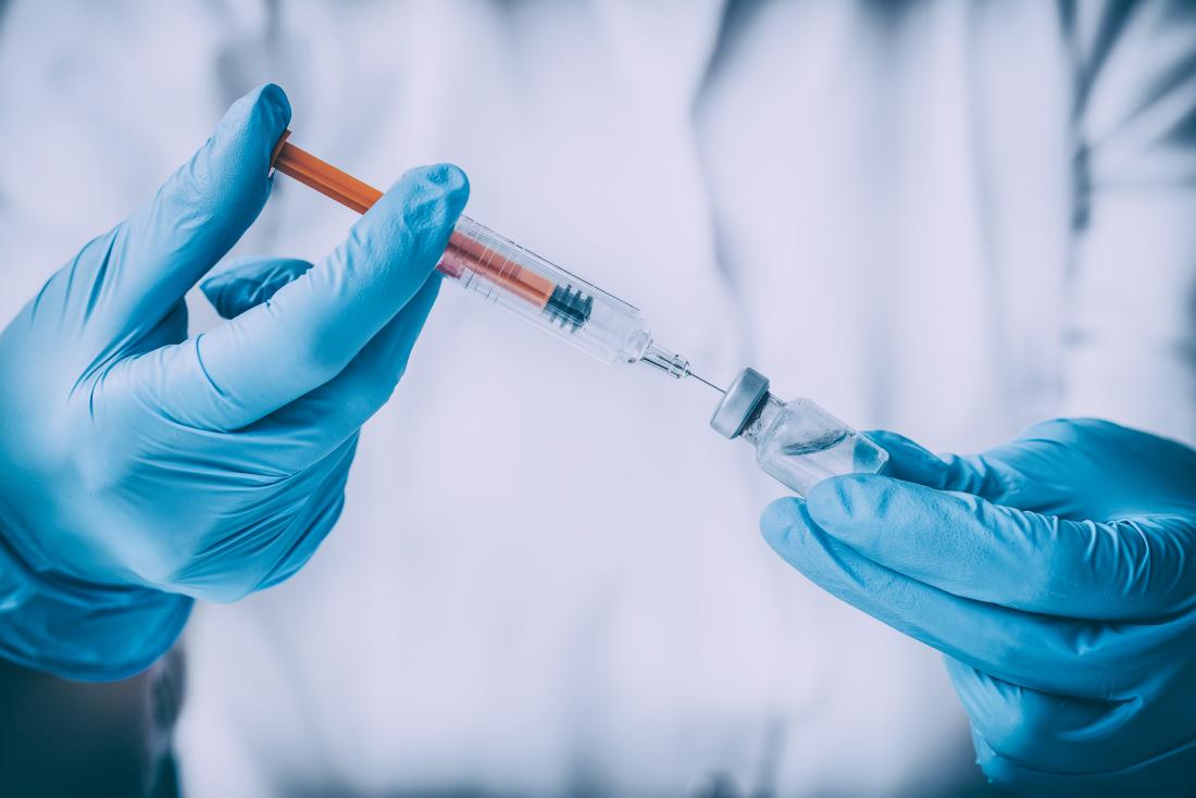 Ubat suntikan vaksin dalam botol yang diambil oleh jarum suntik dalam tangan bersarung.