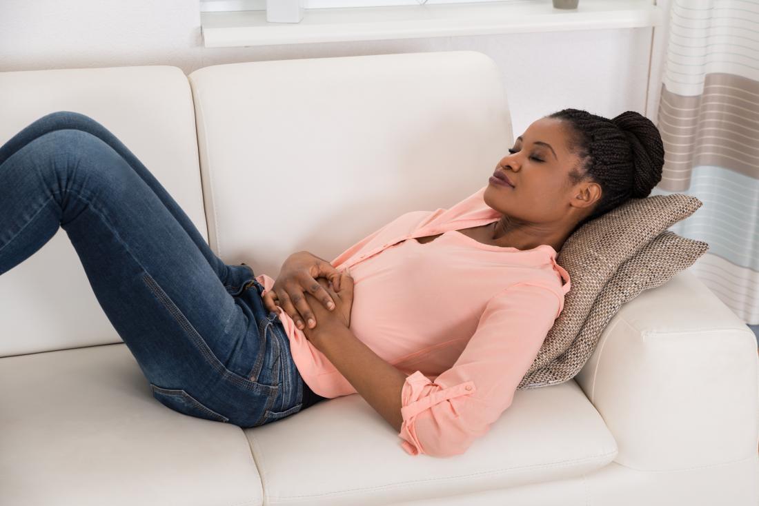 wanita muda berbaring di atas sofa yang ingin tahu bagaimana untuk menghilangkan rasa mual