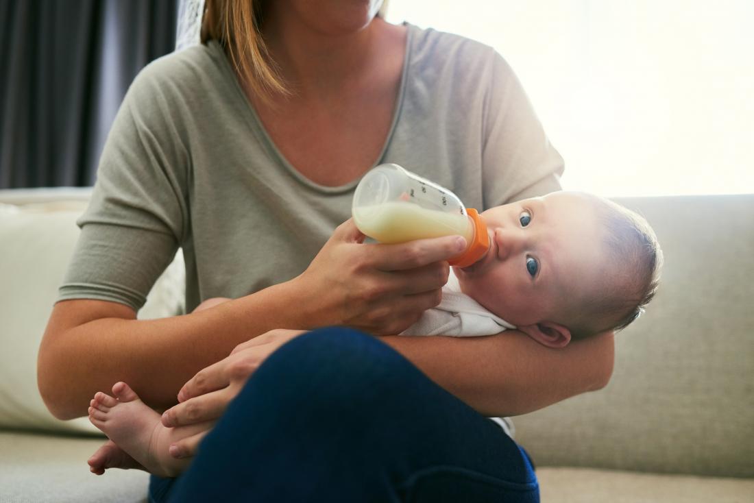 Ibu makan bayi di dalam lengannya dengan botol susu.