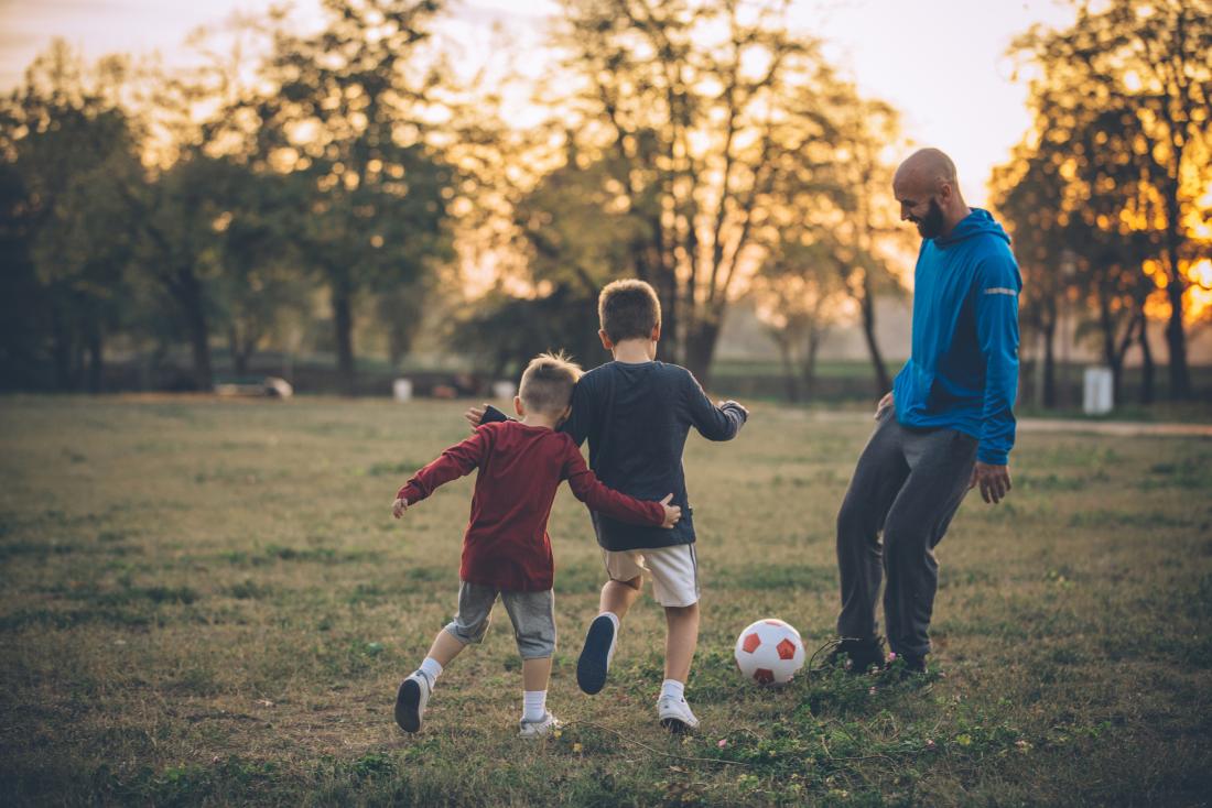 Kanak-kanak bermain bola sepak dengan ayah mereka di taman
